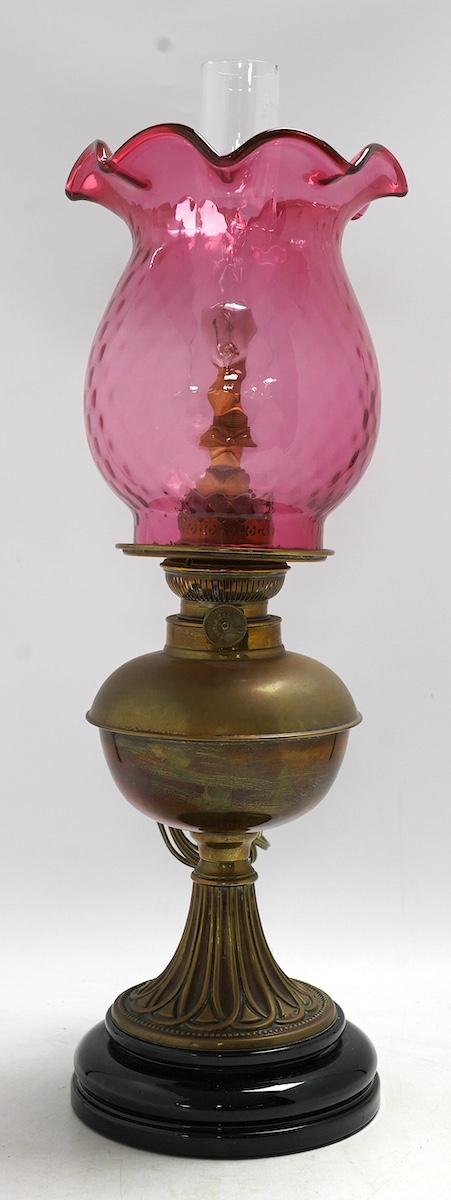 A Victorian brass oil lamp with cranberry glass shade. Condition - fair